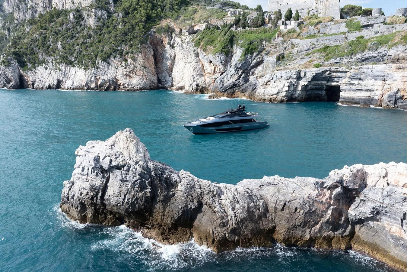 A sleek yacht cruises through a picturesque coastal landscape with rocky cliffs and clear blue waters. aboard RIVA 112 DOLCEVITA SUPER Yacht for Sale