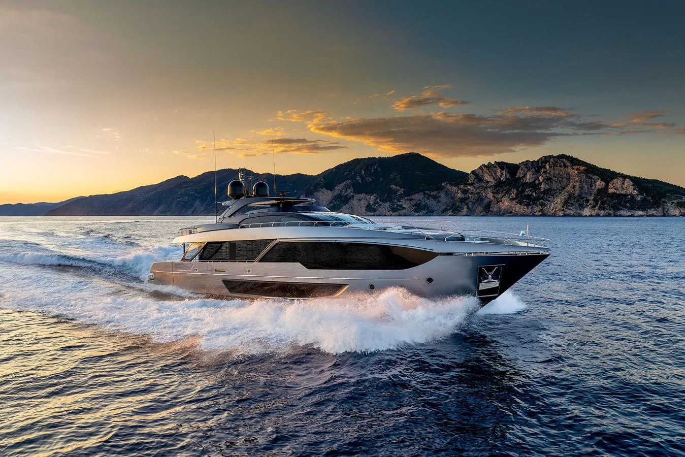 A sleek and modern yacht cruises through the water at sunset, with scenic mountains in the background. aboard RIVA 112 DOLCEVITA SUPER Yacht for Sale