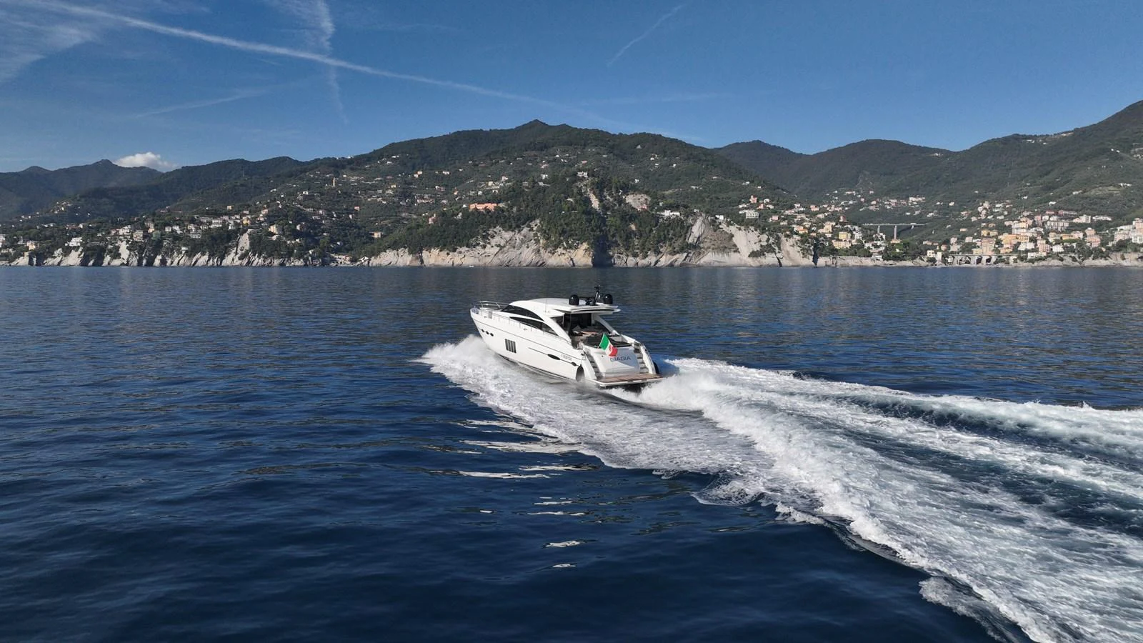 A sleek yacht glides swiftly across calm waters with a scenic coastal backdrop. aboard GIA GIA' Yacht for Sale
