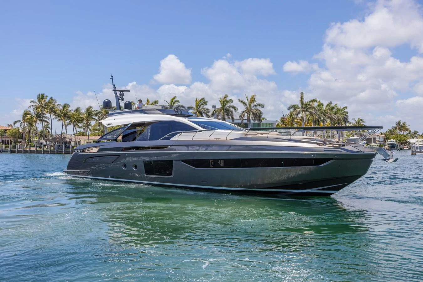 A sleek and modern yacht cruises through clear blue waters with a backdrop of palm trees and a bright sky. aboard NO TIME TO DIE Yacht for Sale