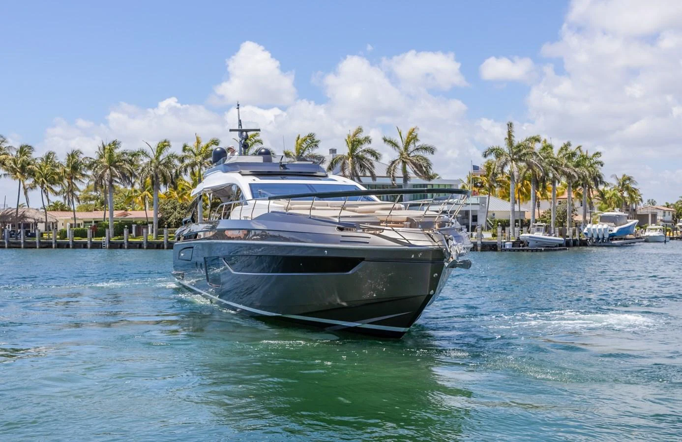 A sleek and modern yacht cruising on a sunny day with palm trees in the background. aboard NO TIME TO DIE Yacht for Sale