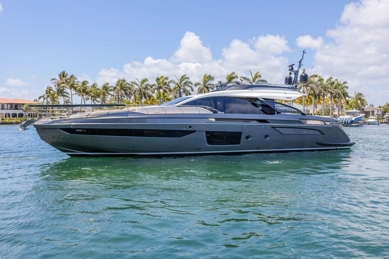 A sleek and modern yacht glides gracefully on the water, set against a backdrop of palm trees and clear skies. aboard NO TIME TO DIE Yacht for Sale