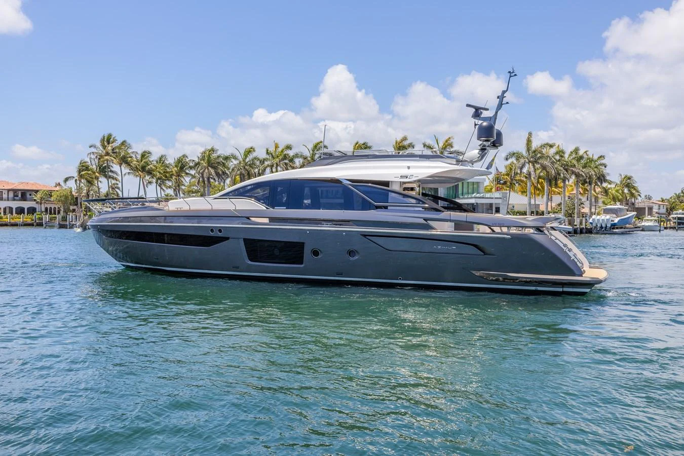 A sleek and modern yacht glides gracefully on calm waters, framed by a picturesque backdrop of palm trees and blue skies. aboard NO TIME TO DIE Yacht for Sale