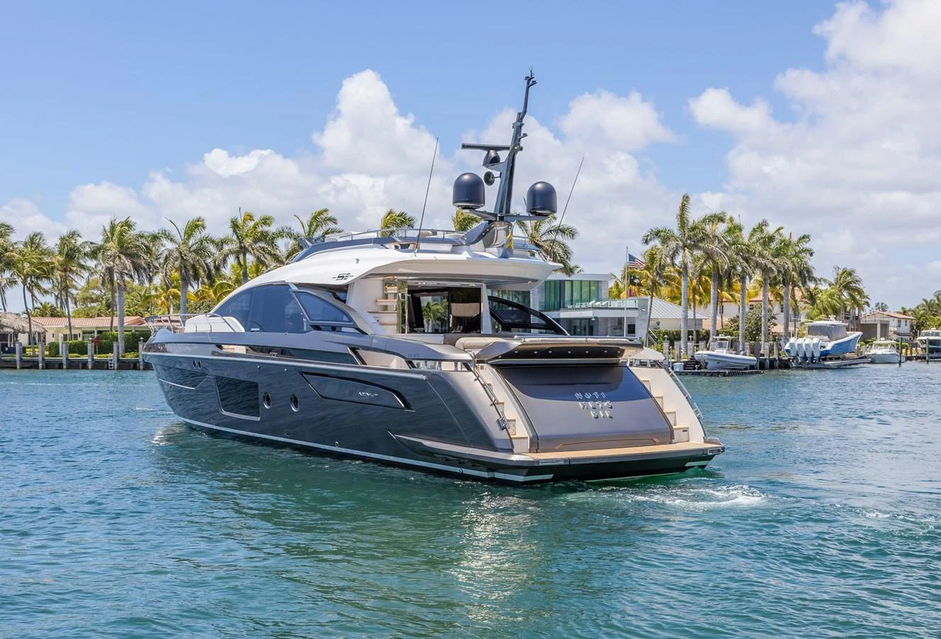 A sleek and modern yacht cruises through a serene waterfront setting with palm trees in the background. aboard NO TIME TO DIE Yacht for Sale