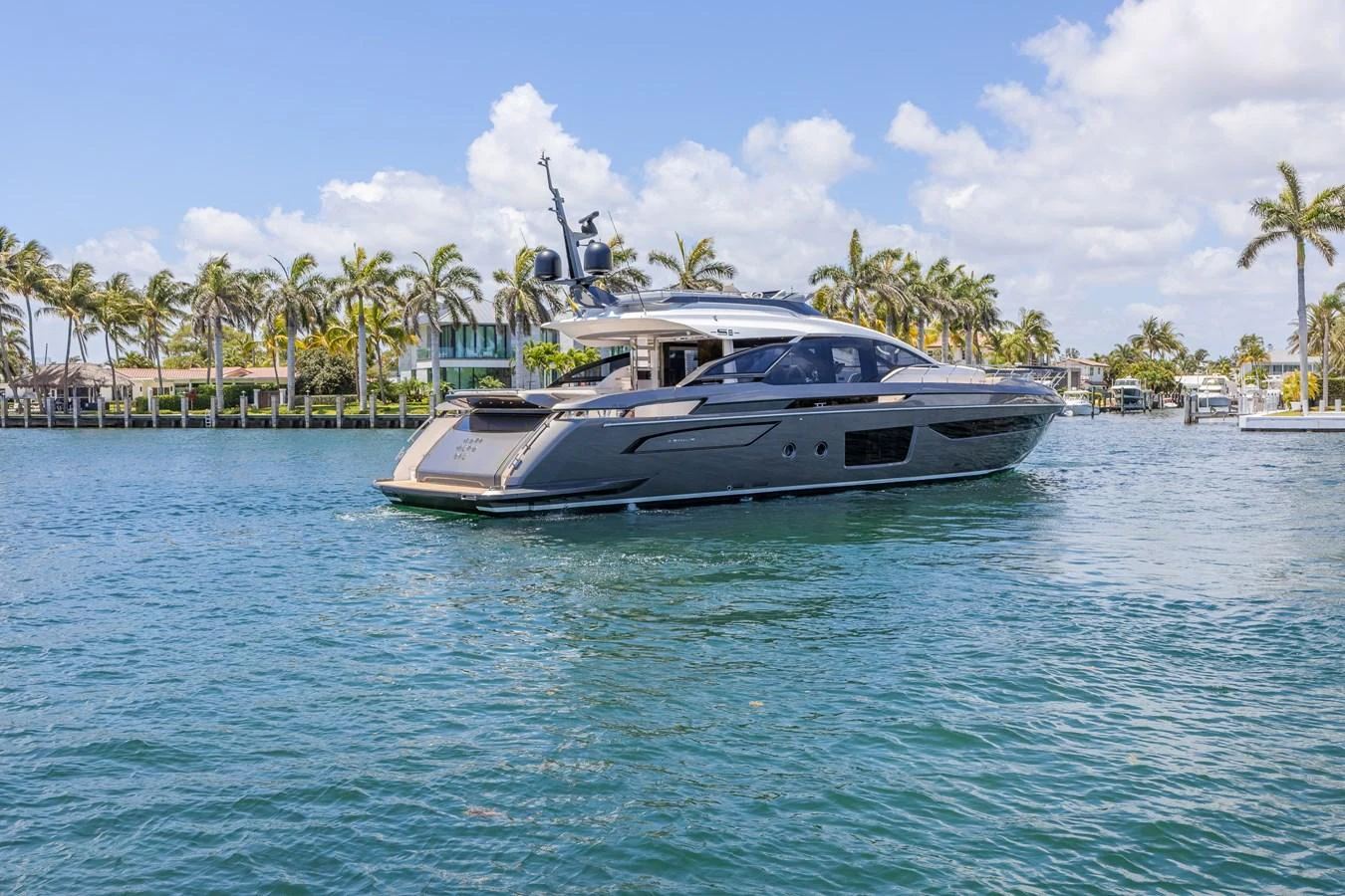 A sleek and modern yacht cruises through calm, tropical waters with palm trees in the background. aboard NO TIME TO DIE Yacht for Sale