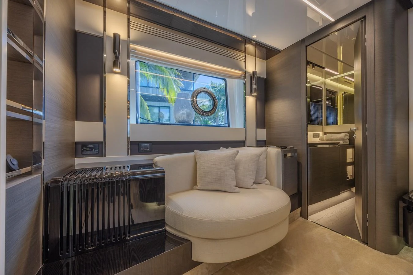 The yacht's interior features a cozy seating area with modern design elements and a view through a porthole window. aboard NO TIME TO DIE Yacht for Sale