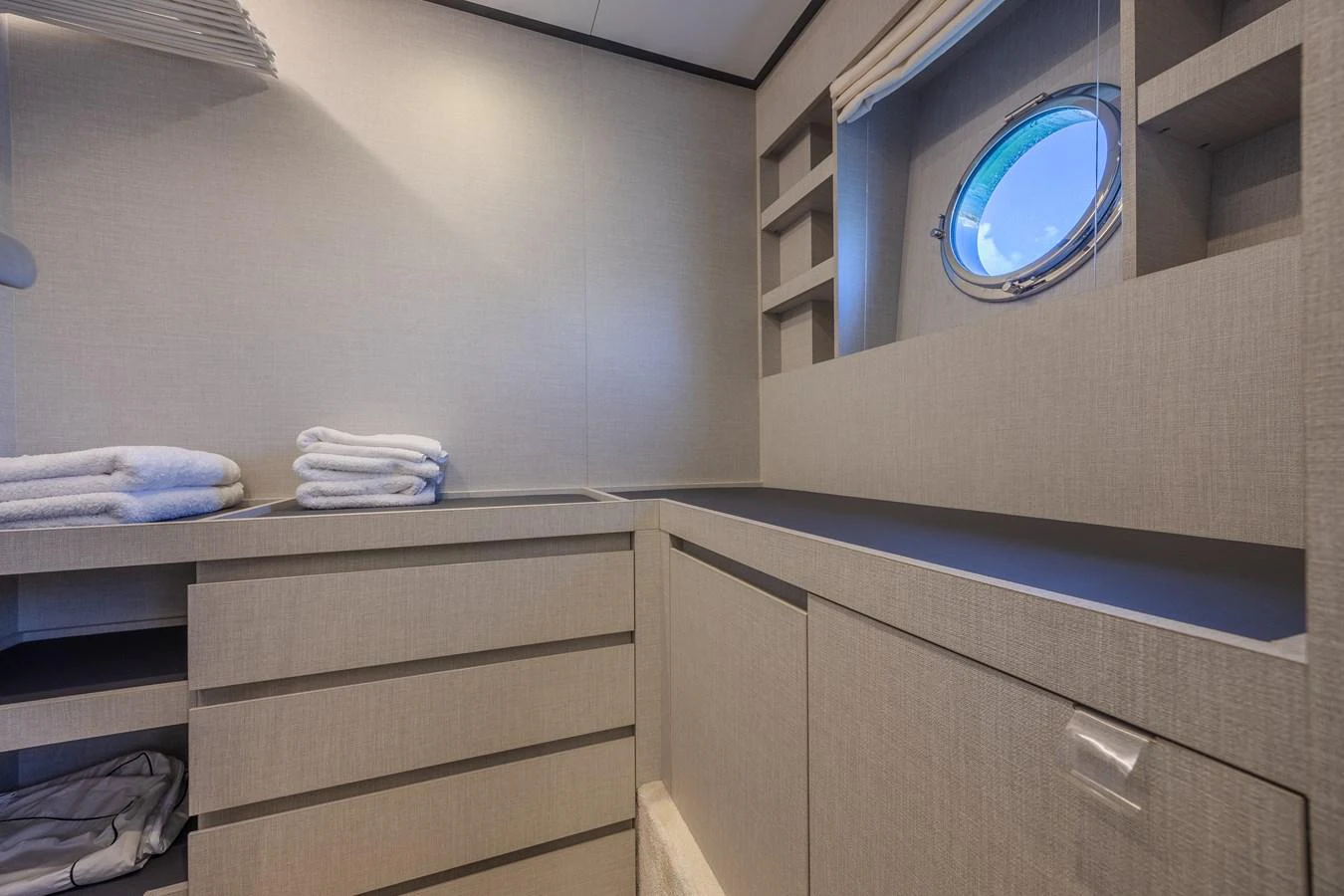 A well-organized storage area with a porthole window, featuring ample shelving and neatly folded towels. aboard NO TIME TO DIE Yacht for Sale