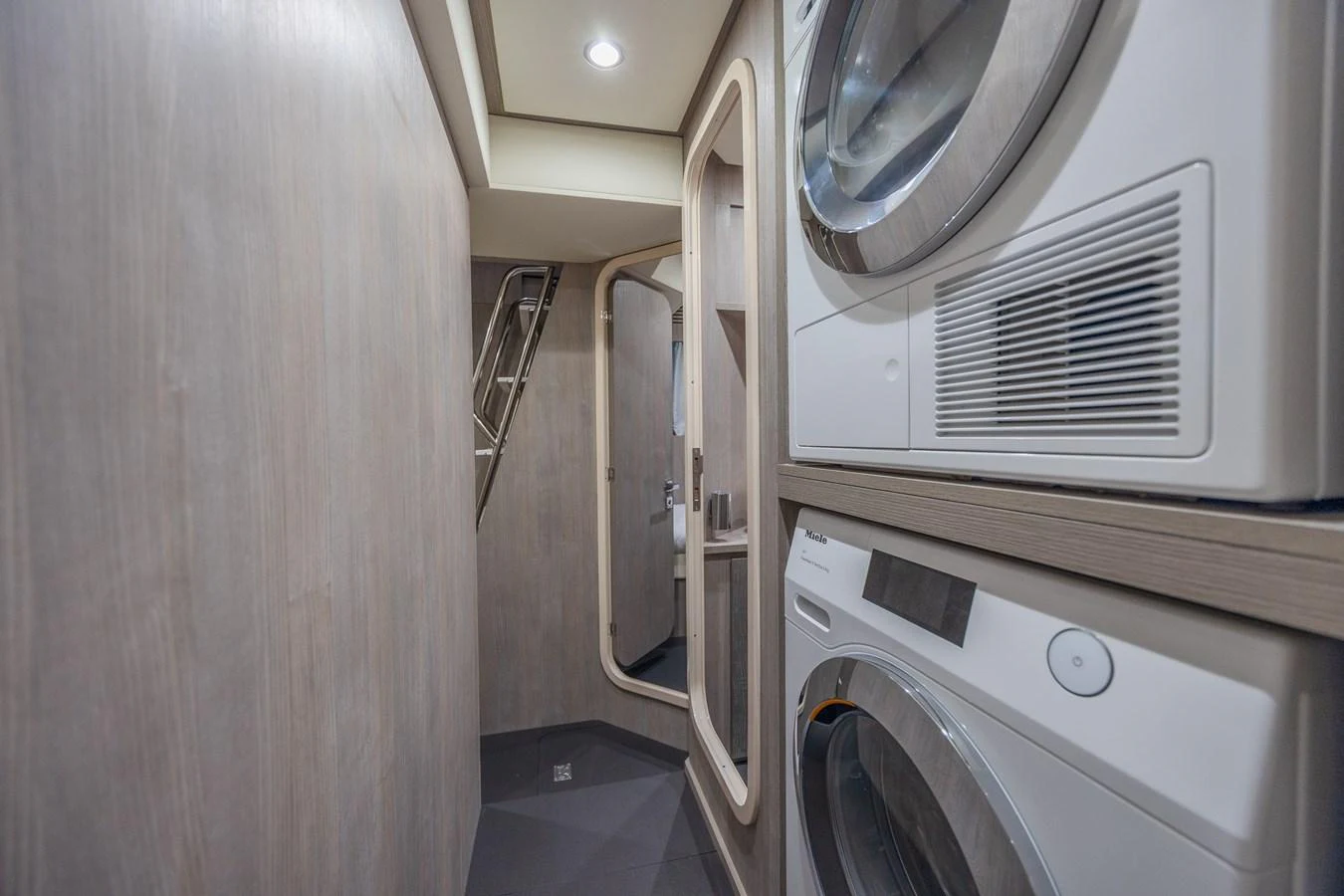 The yacht features a modern laundry room with stacked washer and dryer units. aboard NO TIME TO DIE Yacht for Sale