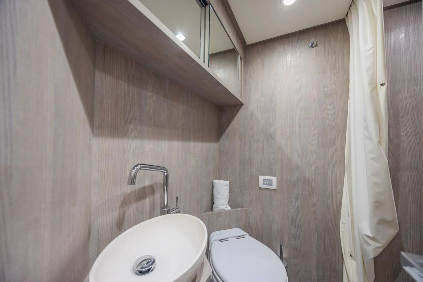 A modern yacht bathroom featuring a sleek sink and toilet with wood paneling. aboard NO TIME TO DIE Yacht for Sale