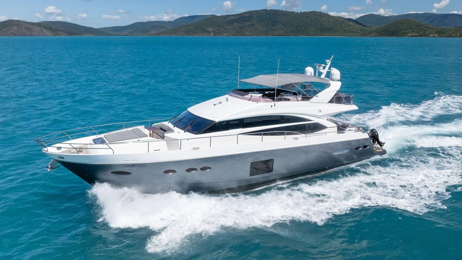 A sleek and modern yacht cruising through clear blue waters with scenic hills in the background. aboard ABOUT TIME Yacht for Sale