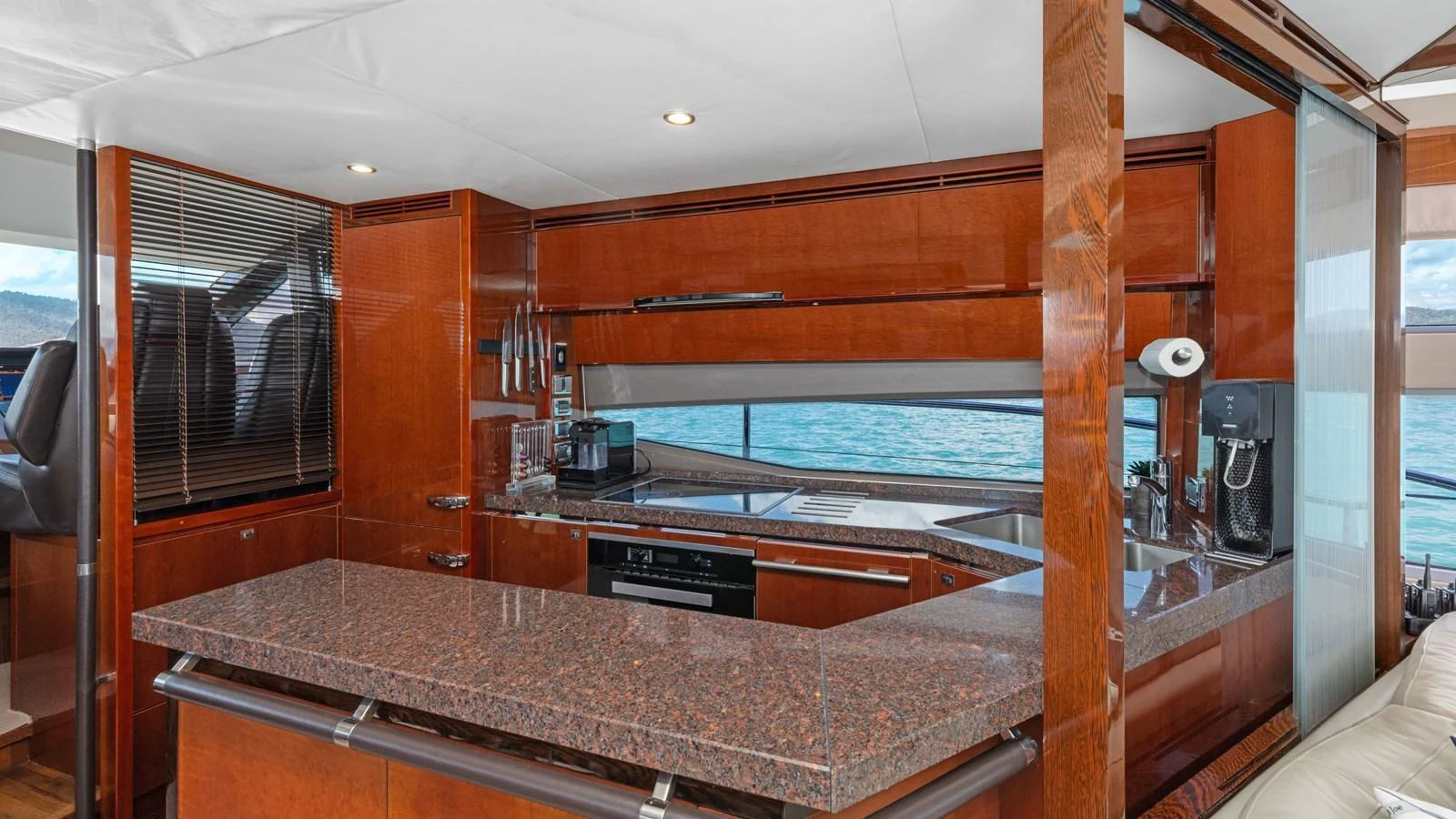 The galley features rich wood cabinetry, modern appliances, and a large granite countertop with a view of the sea. aboard ABOUT TIME Yacht for Sale