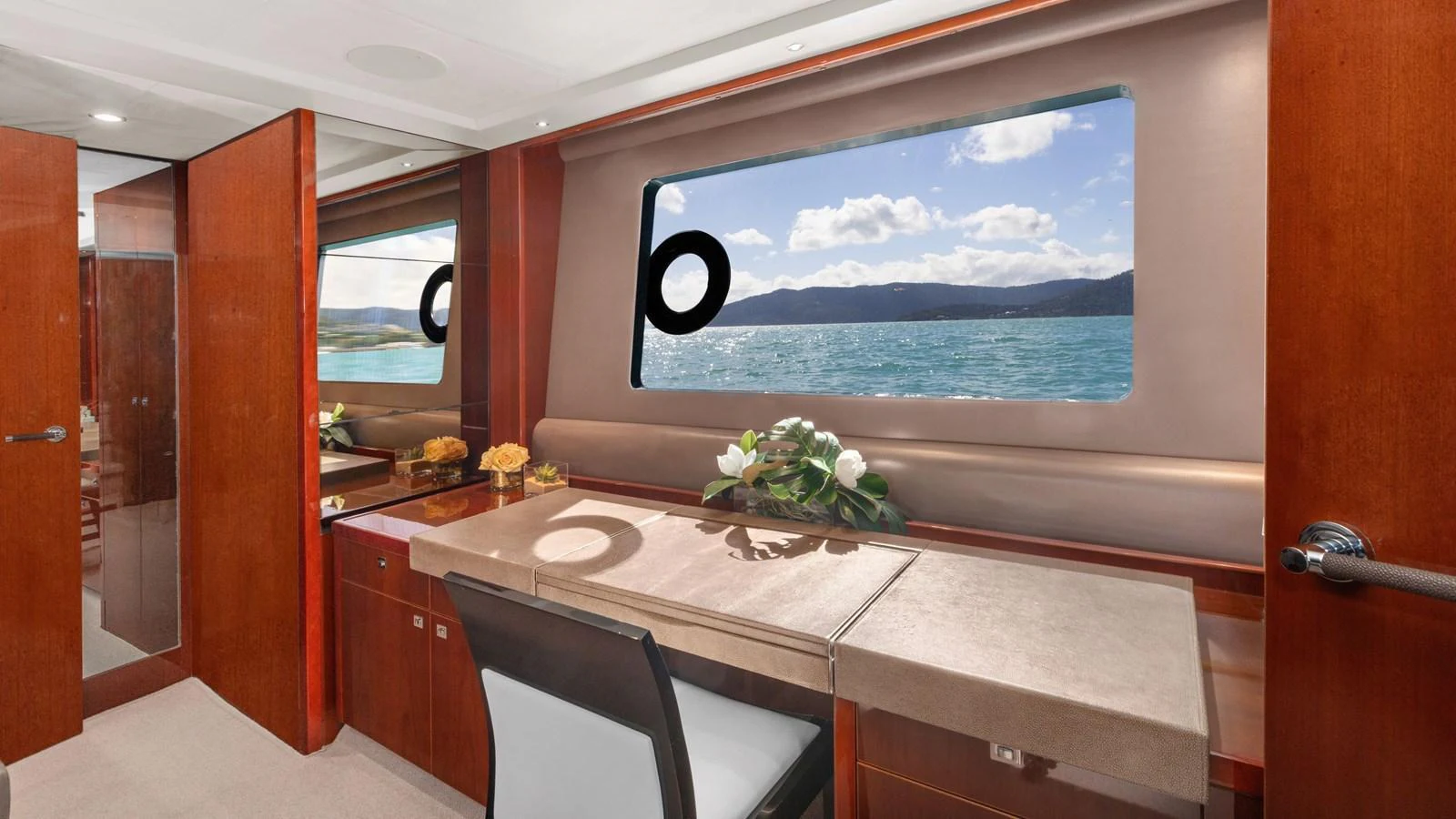 The yacht's interior features a well-appointed workspace with a scenic ocean view through large windows. aboard ABOUT TIME Yacht for Sale