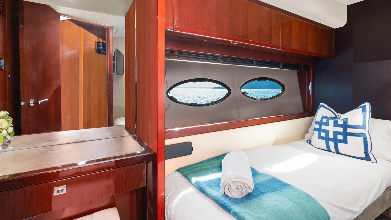 The cozy stateroom features a comfortable bed with a view of the sea through oval windows. aboard ABOUT TIME Yacht for Sale