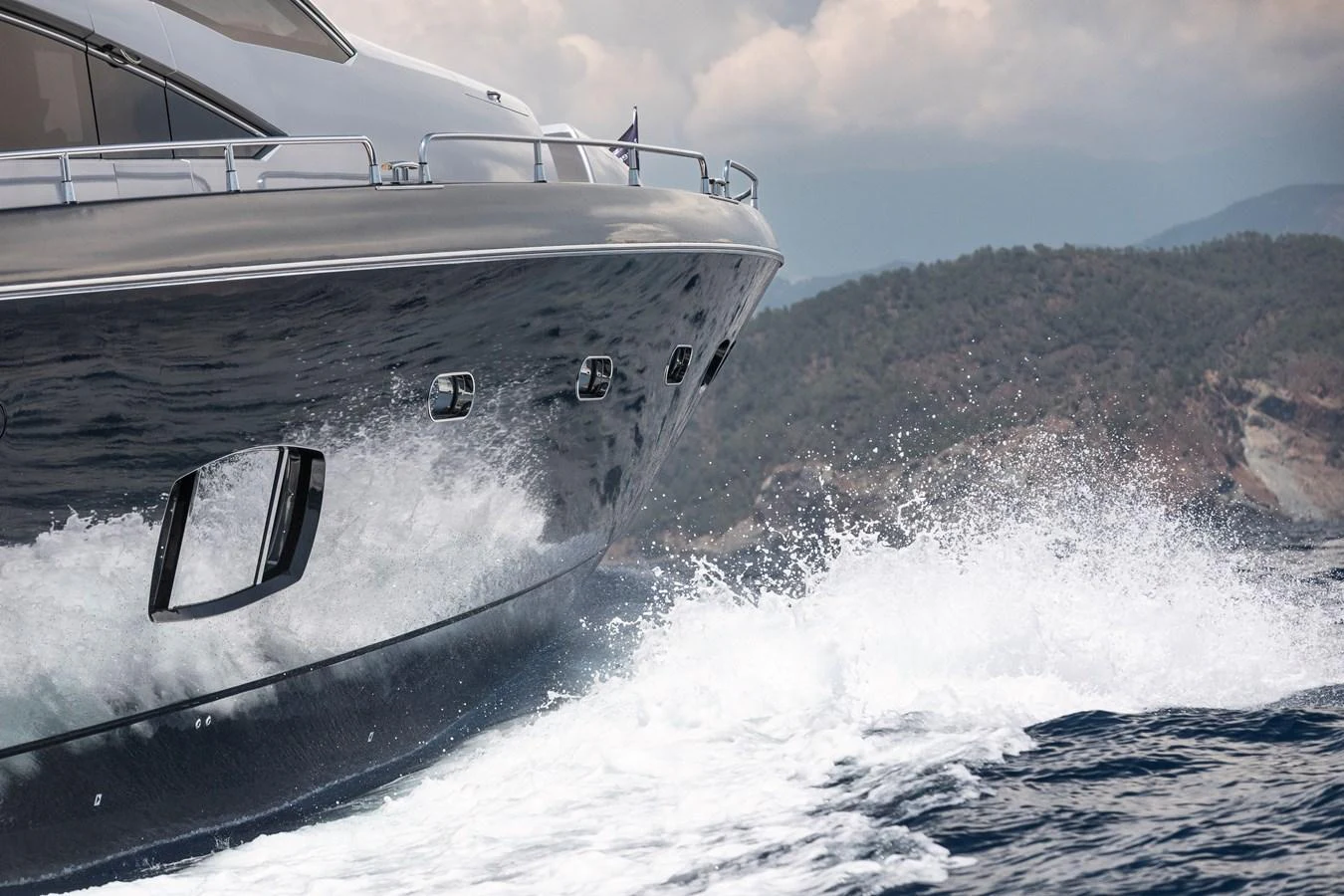 The yacht cuts through the waves with a stunning backdrop of rugged coastline and cloudy skies. aboard AMARA Yacht for Sale