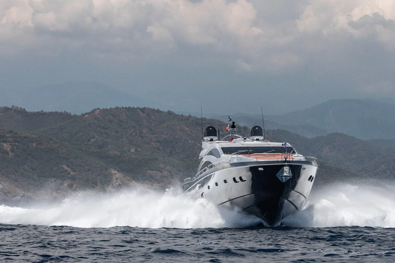 A sleek yacht cruises powerfully through the water against a backdrop of rugged hills. aboard AMARA Yacht for Sale