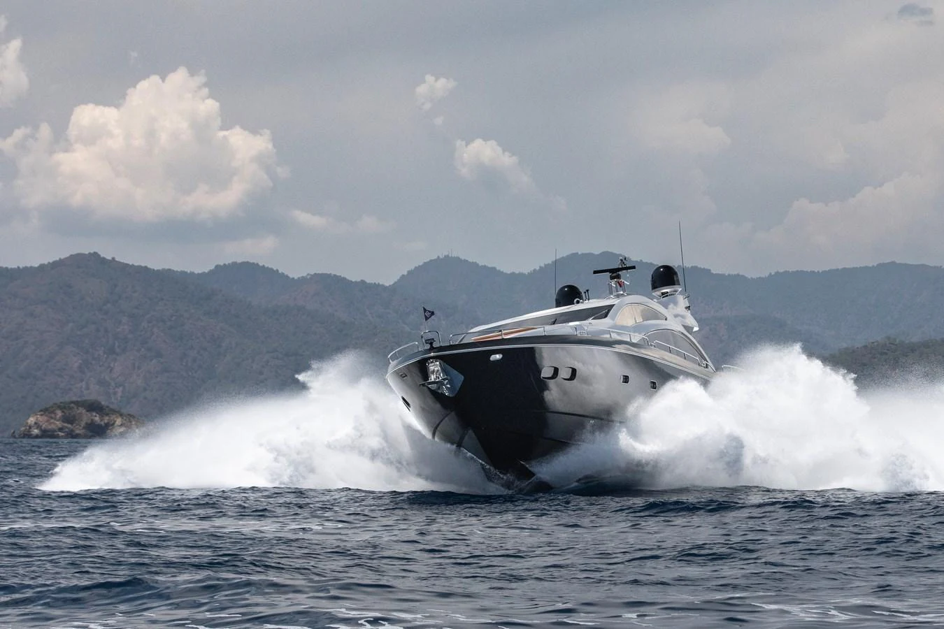 A sleek yacht powers through the waves against a backdrop of scenic mountains. aboard AMARA Yacht for Sale