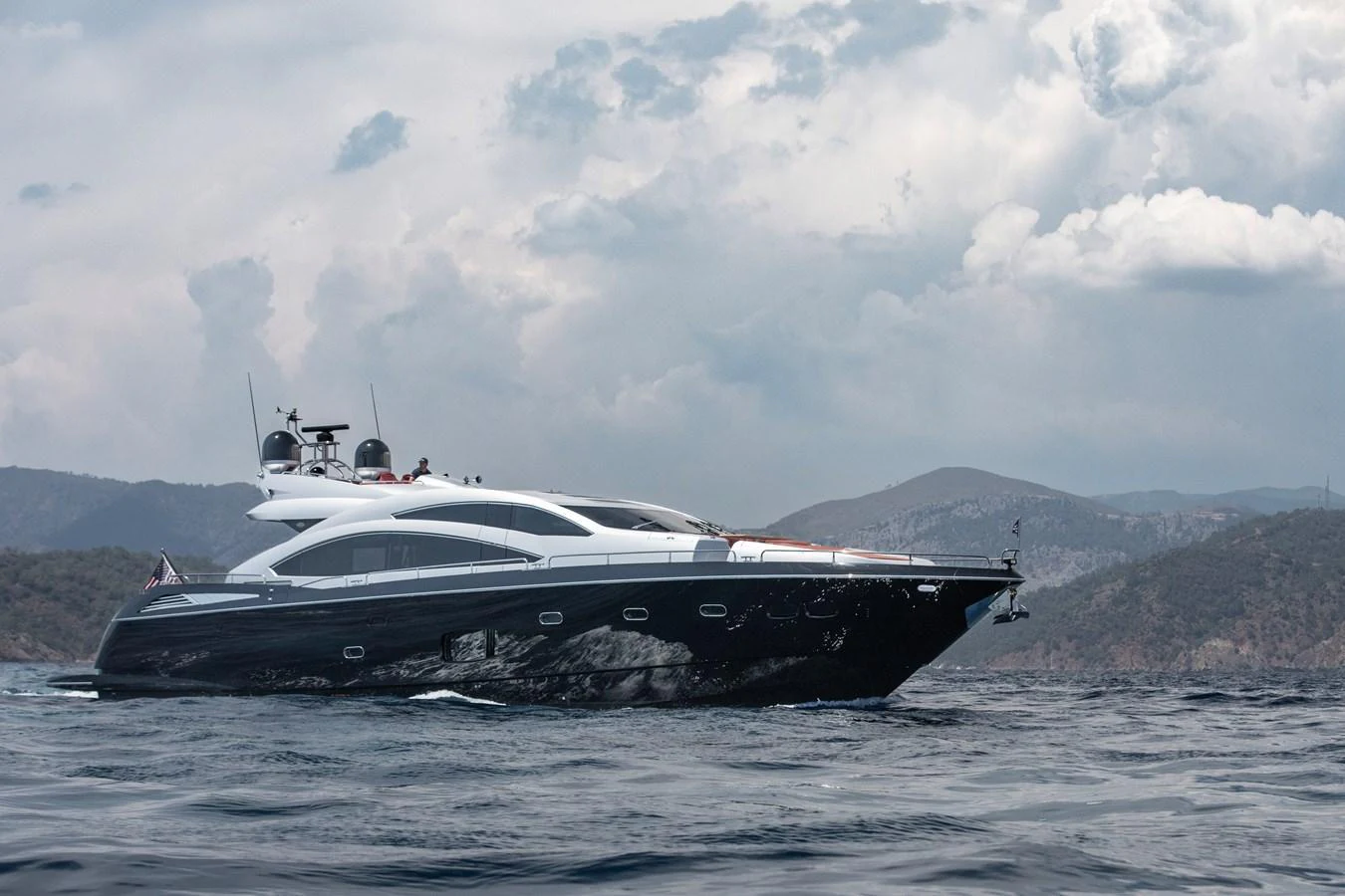 A sleek and modern yacht cruises gracefully on the open water against a backdrop of scenic mountains. aboard AMARA Yacht for Sale