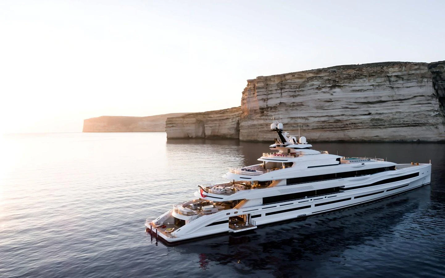 A luxurious yacht is anchored near stunning cliffs at sunset, showcasing its sleek design and expansive decks. aboard LANA Yacht for Sale