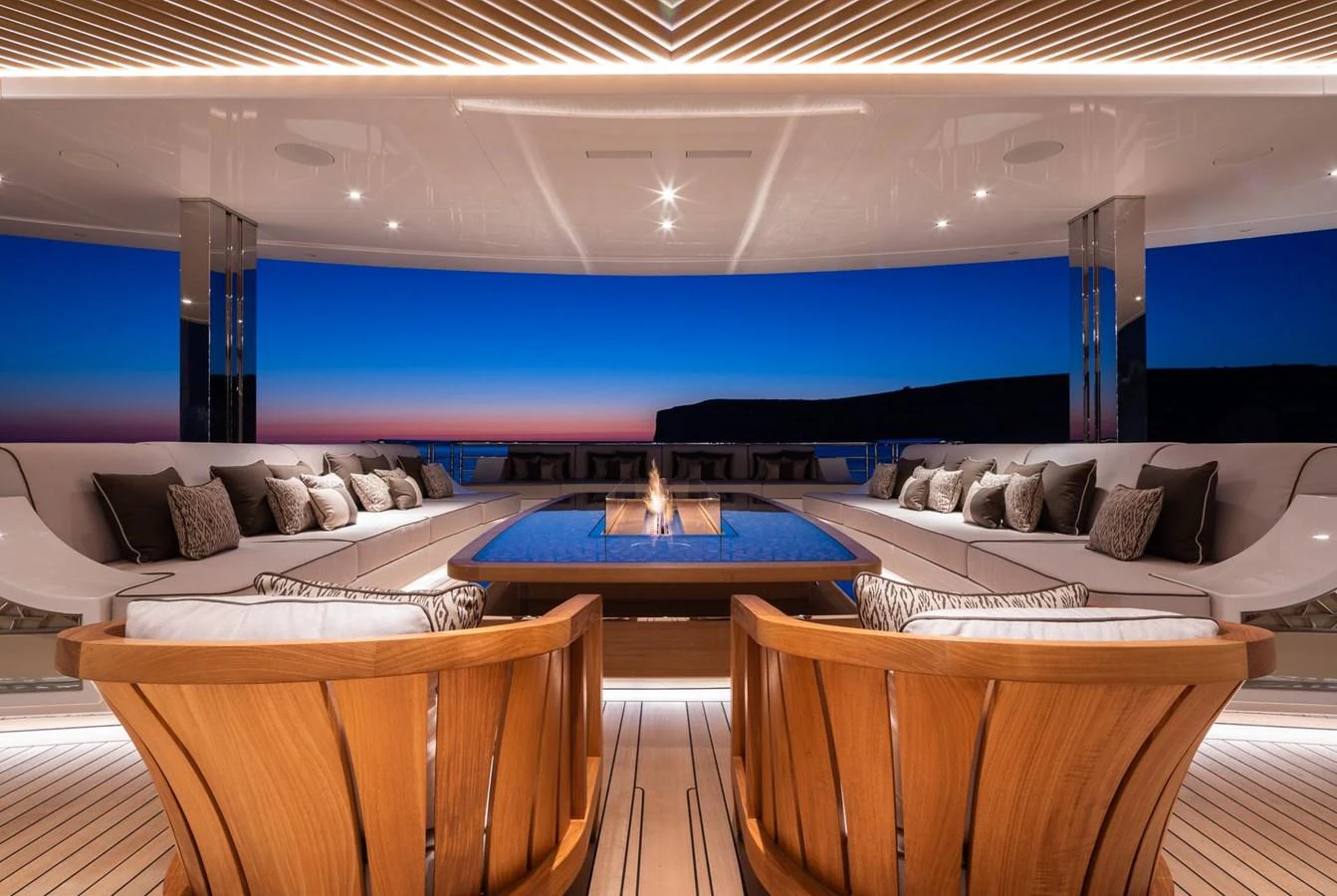 The yacht features a luxurious lounge area with a central fire pit, surrounded by plush seating and elegant wooden chairs, perfect for evening relaxation. aboard LANA Yacht for Sale