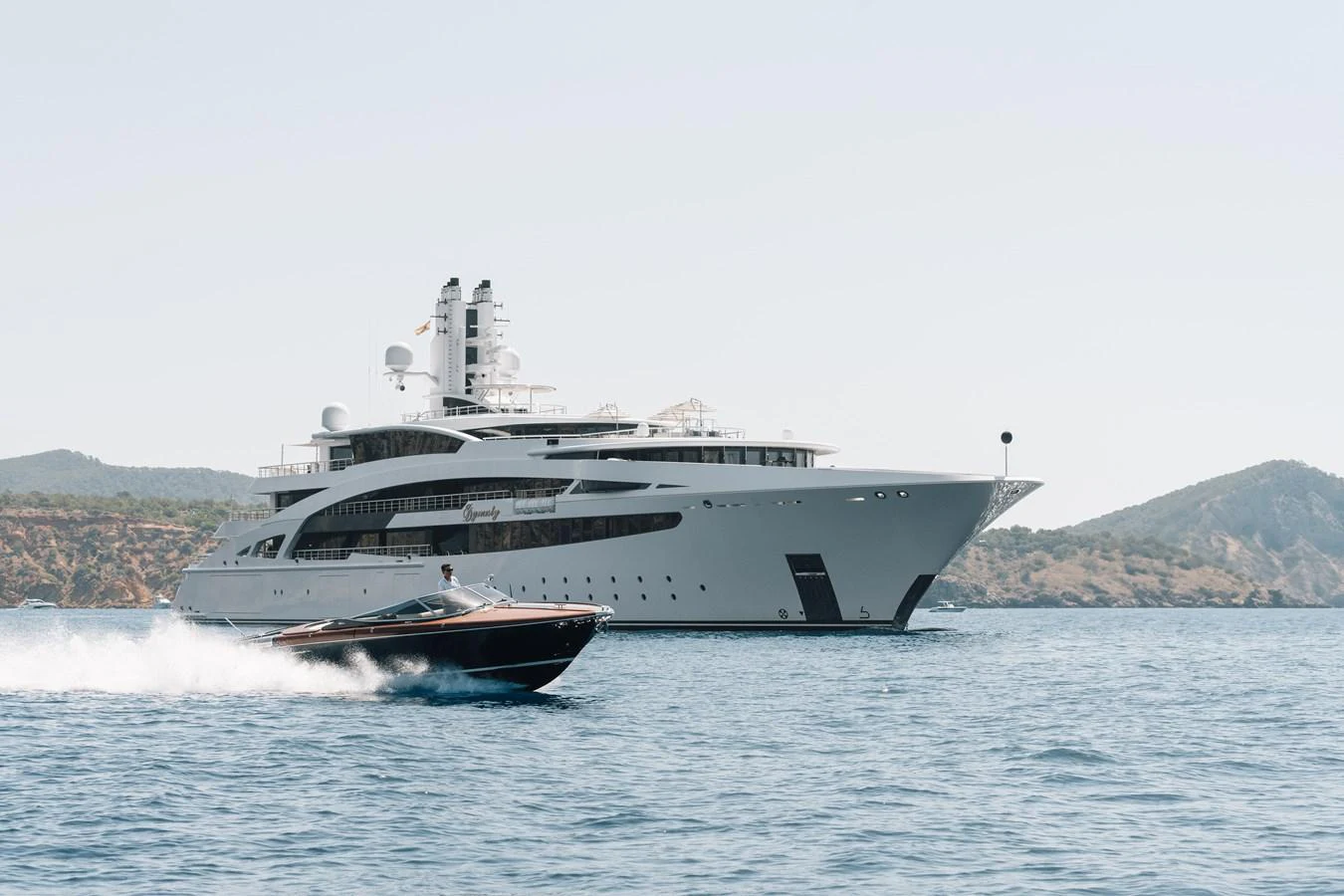 A sleek, modern yacht glides through calm waters with a scenic coastline in the background. aboard I DYNASTY Yacht for Sale