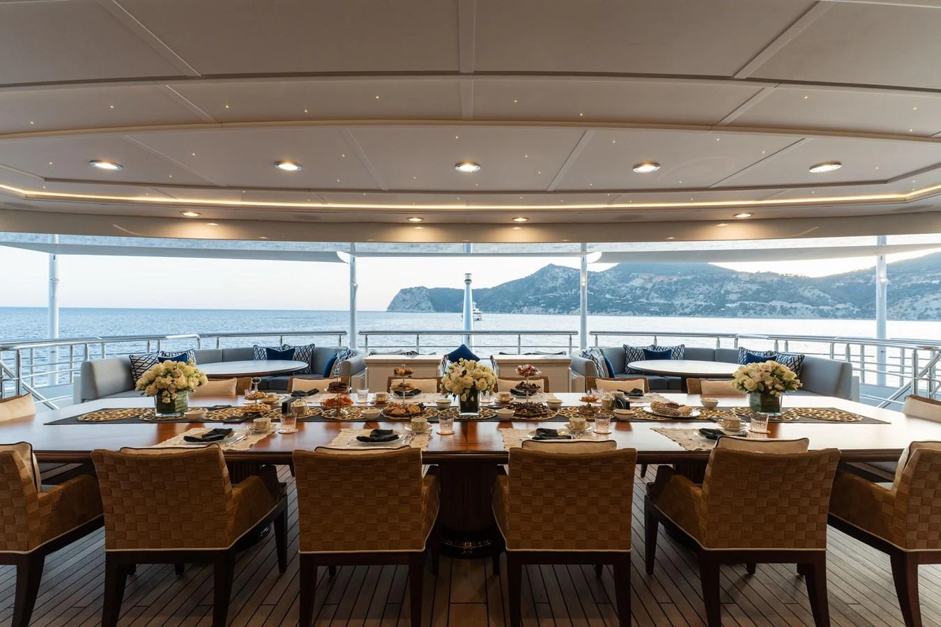 An elegant aft deck dining area with a large table set for a meal, offering stunning sea views. aboard I DYNASTY Yacht for Sale