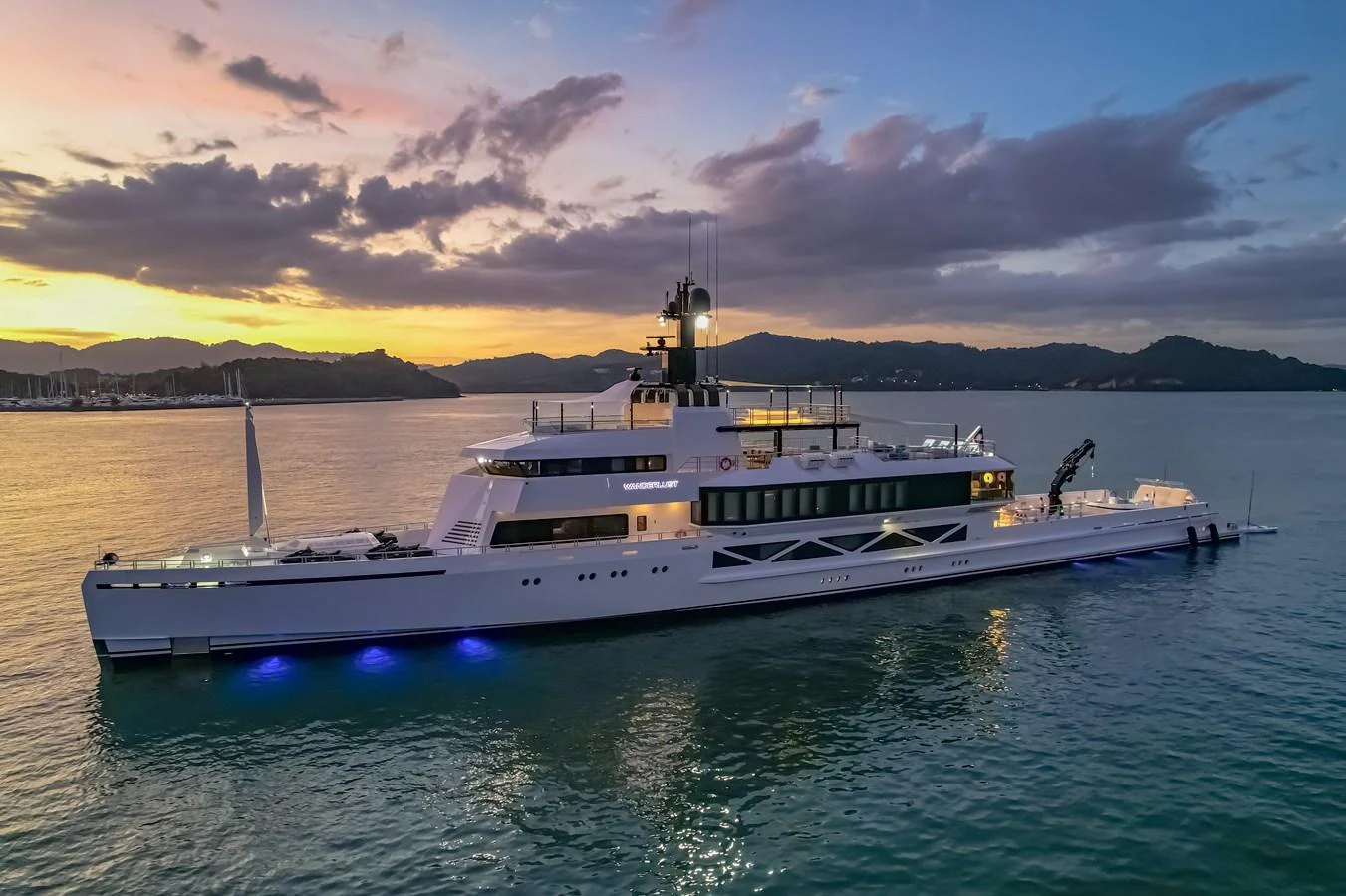 A sleek and modern yacht is illuminated against a stunning sunset backdrop on calm waters. aboard WANDERLUST Yacht for Sale
