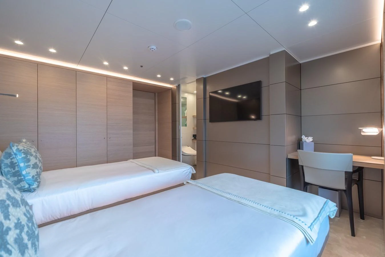 The guest stateroom features twin beds, a flat-screen TV, and a work desk, offering a comfortable and modern retreat. aboard WANDERLUST Yacht for Sale