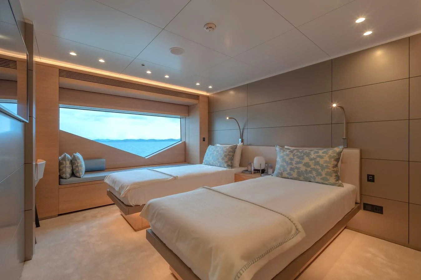The guest stateroom features twin beds, modern lighting, and a large window with an ocean view. aboard WANDERLUST Yacht for Sale
