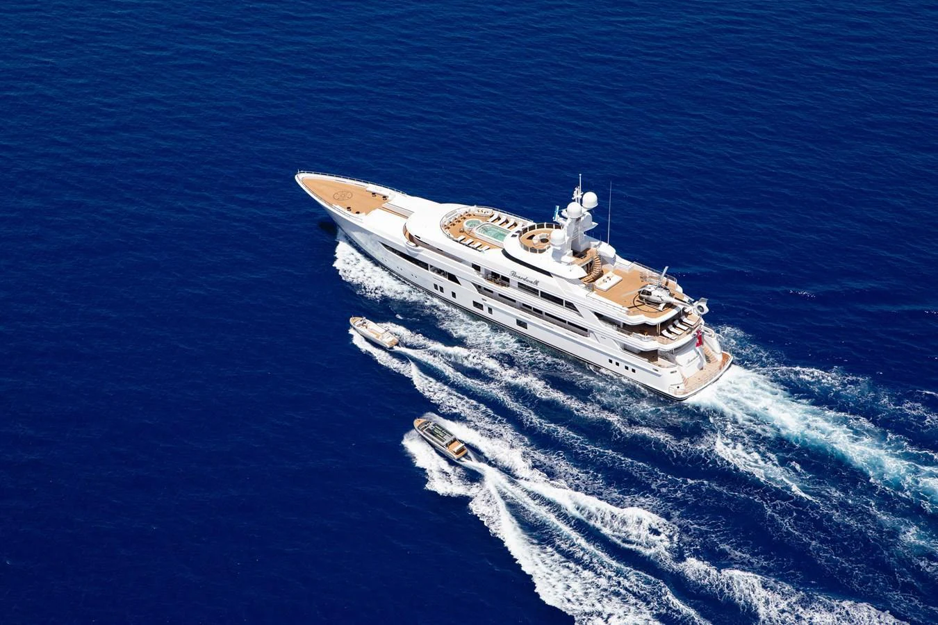 A luxurious yacht cruises through the deep blue sea, accompanied by two tenders. aboard BOARDWALK V Yacht for Sale