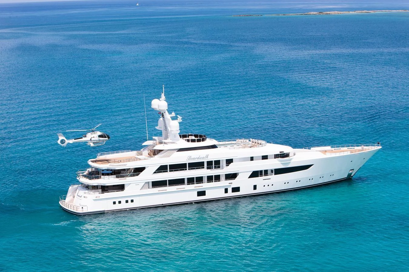 A stunning yacht cruising in clear blue waters, accompanied by a helicopter on its deck. aboard BOARDWALK V Yacht for Sale