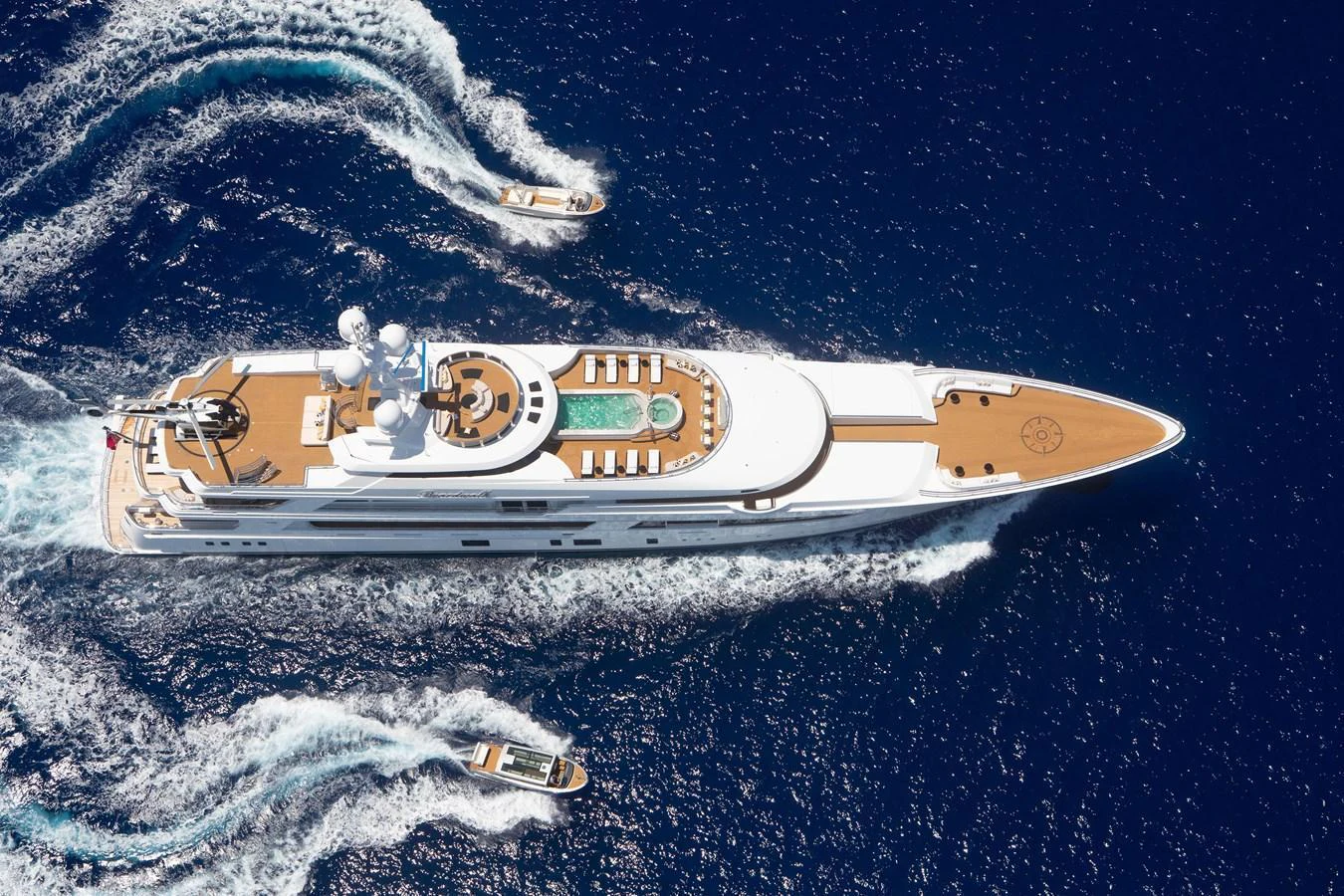 A stunning aerial view of a luxurious yacht cruising through deep blue waters, accompanied by tenders. aboard BOARDWALK V Yacht for Sale