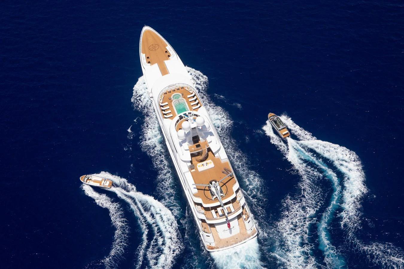 A stunning aerial view of a luxurious yacht cruising through deep blue waters, accompanied by three tenders. aboard BOARDWALK V Yacht for Sale