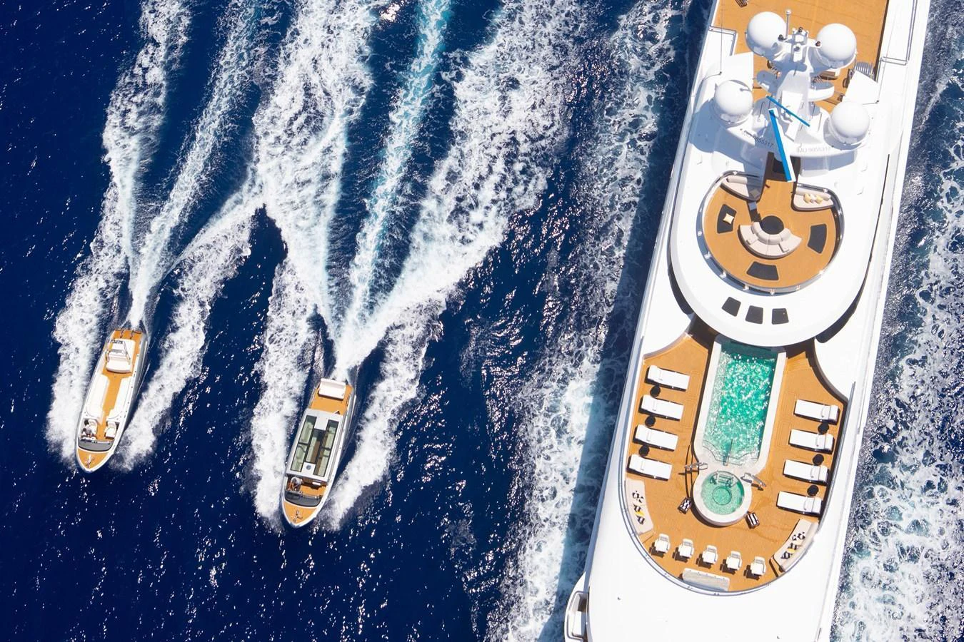 A luxurious yacht cruising with two tenders on a vibrant blue sea, showcasing a spacious sundeck with a pool. aboard BOARDWALK V Yacht for Sale