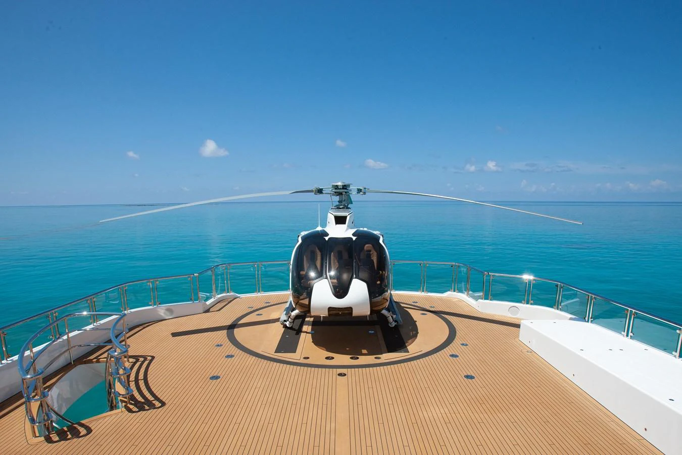 The yacht features a spacious helipad with a helicopter ready for takeoff, set against a stunning ocean backdrop. aboard BOARDWALK V Yacht for Sale