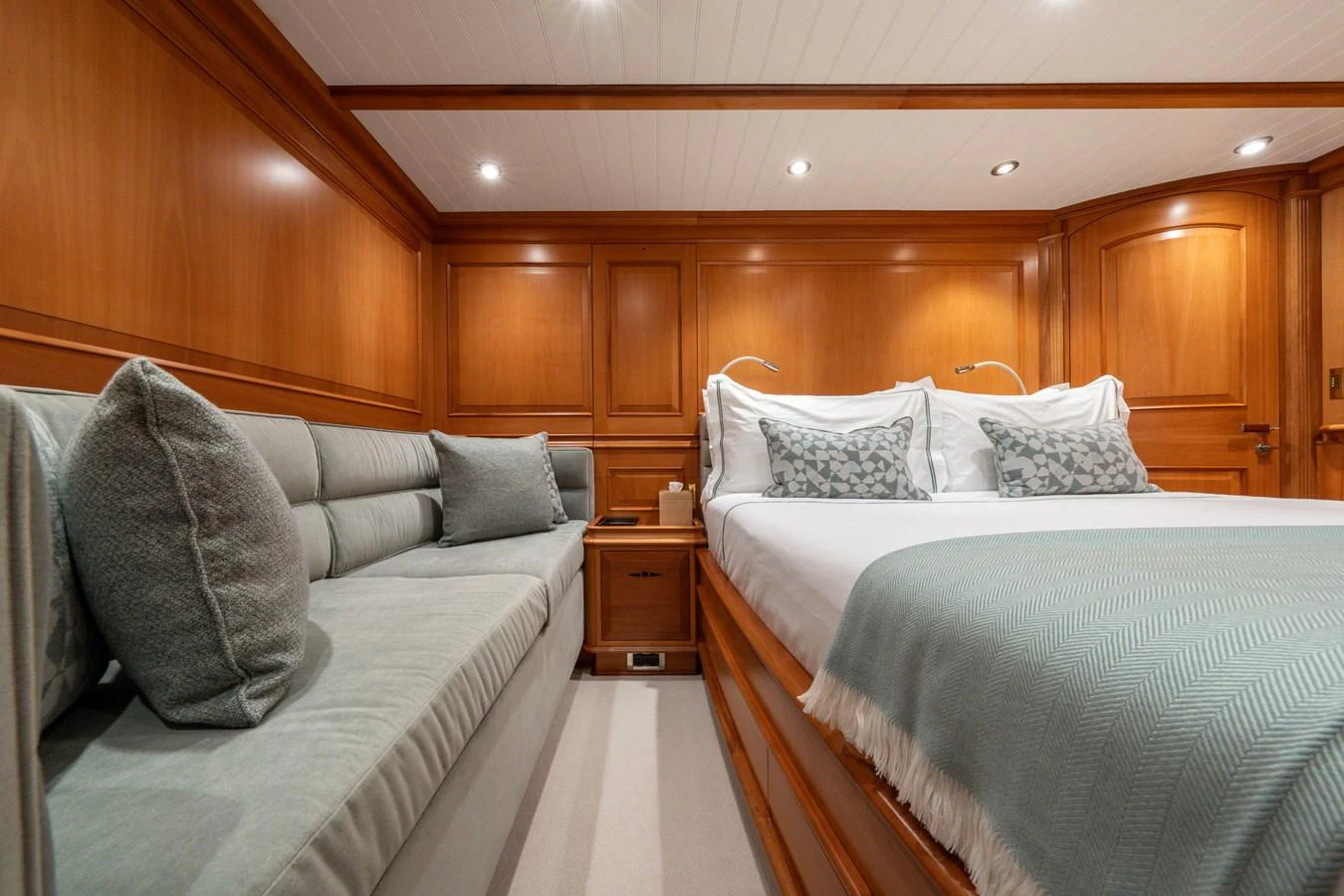 The stateroom features a cozy bed with plush pillows and a comfortable sofa, all set against elegant wooden paneling. aboard ATHOS Yacht for Sale