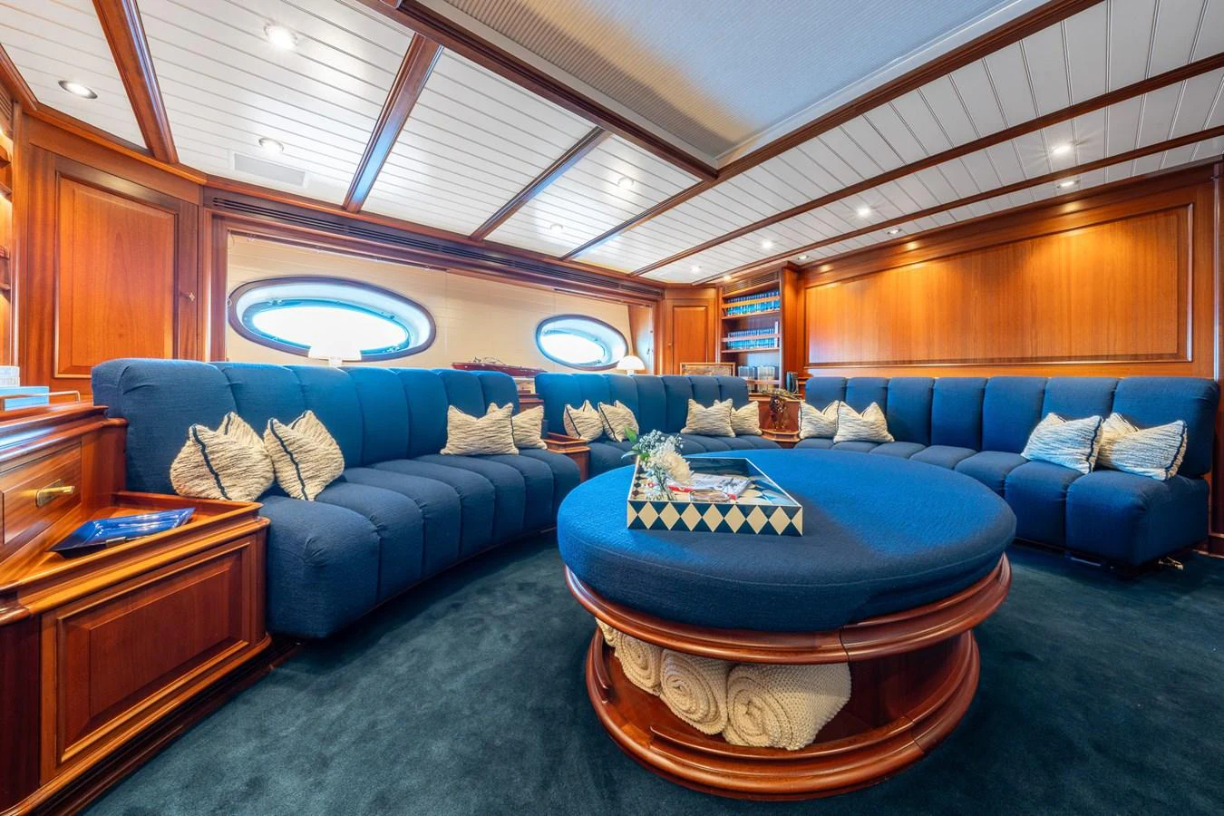 The salon features plush blue seating and elegant wooden accents, creating a cozy and luxurious atmosphere. aboard ATHOS Yacht for Sale