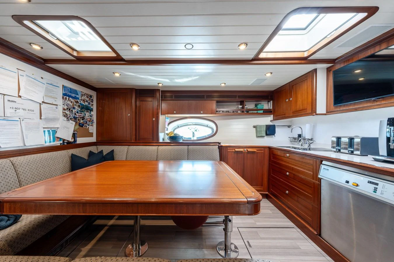 The yacht's dining area features a spacious table with ample seating, surrounded by rich wooden cabinetry and modern amenities. aboard ATHOS Yacht for Sale