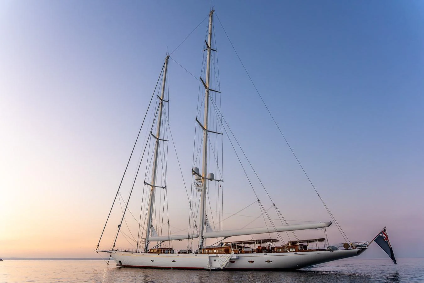 A stunning sailing yacht with tall masts gracefully glides on calm waters at sunset. aboard ATHOS Yacht for Sale