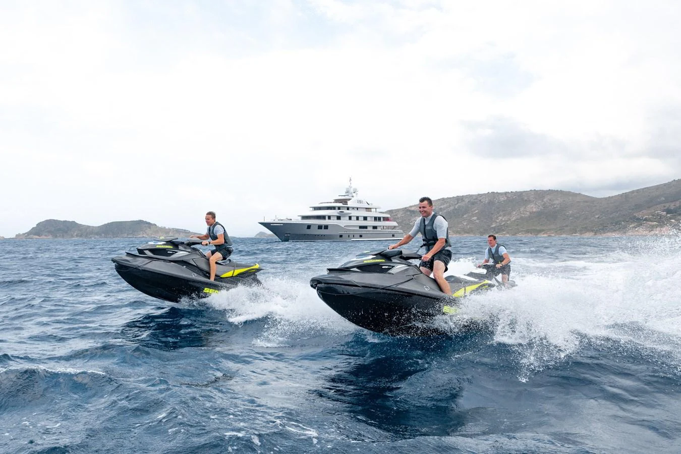 Three people ride jet skis on the water with a large yacht in the background. aboard BATON ROUGE Yacht for Sale