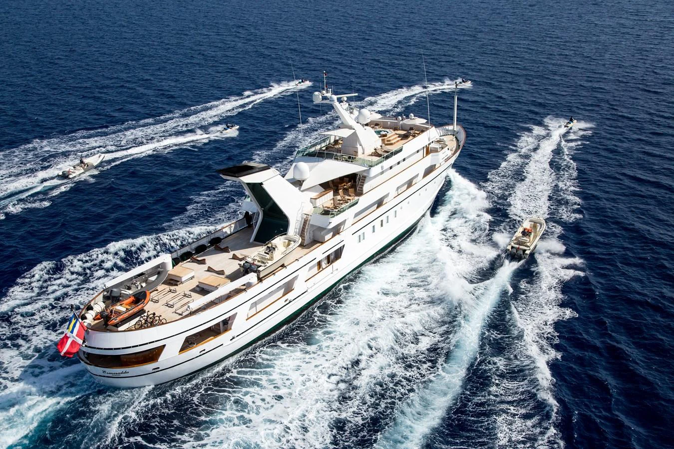 A luxurious yacht cruises through the open sea, accompanied by several smaller boats. aboard ESMERALDA Yacht for Sale