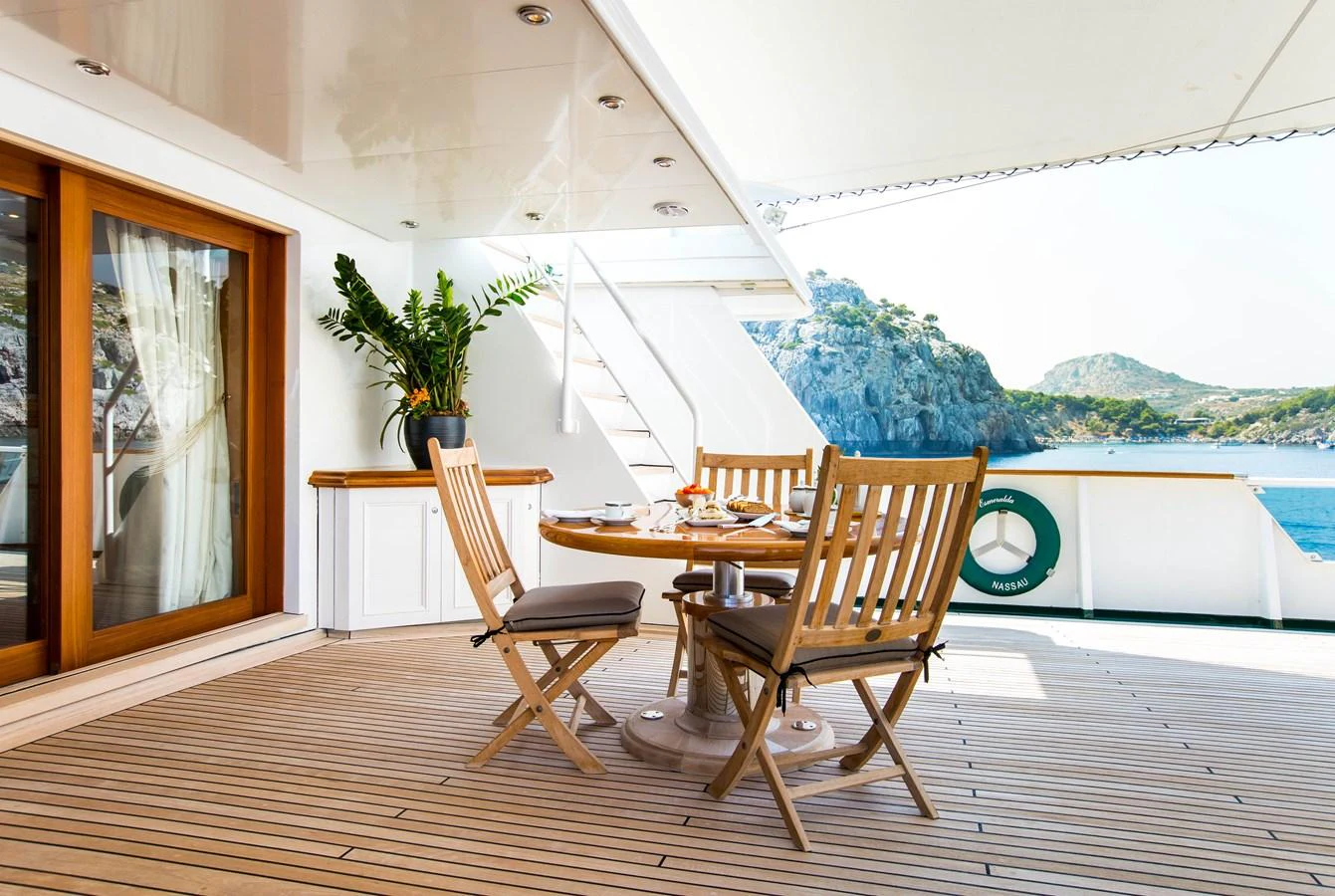 The aft deck features a cozy dining area with wooden chairs and a table, offering stunning views of the surrounding landscape. aboard ESMERALDA Yacht for Sale