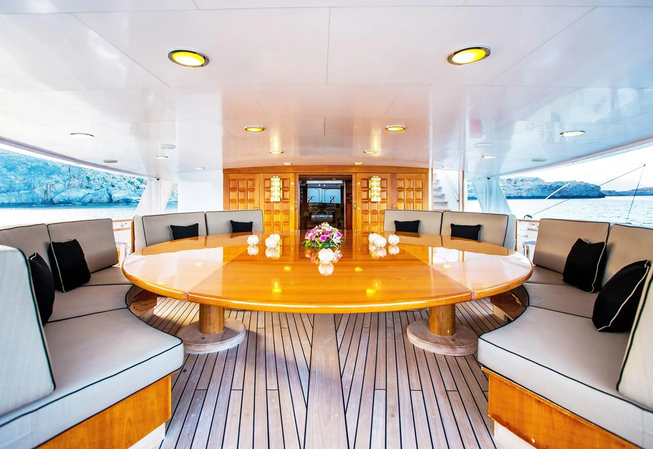 The aft deck features a spacious and elegant dining area with a large wooden table and comfortable seating. aboard ESMERALDA Yacht for Sale