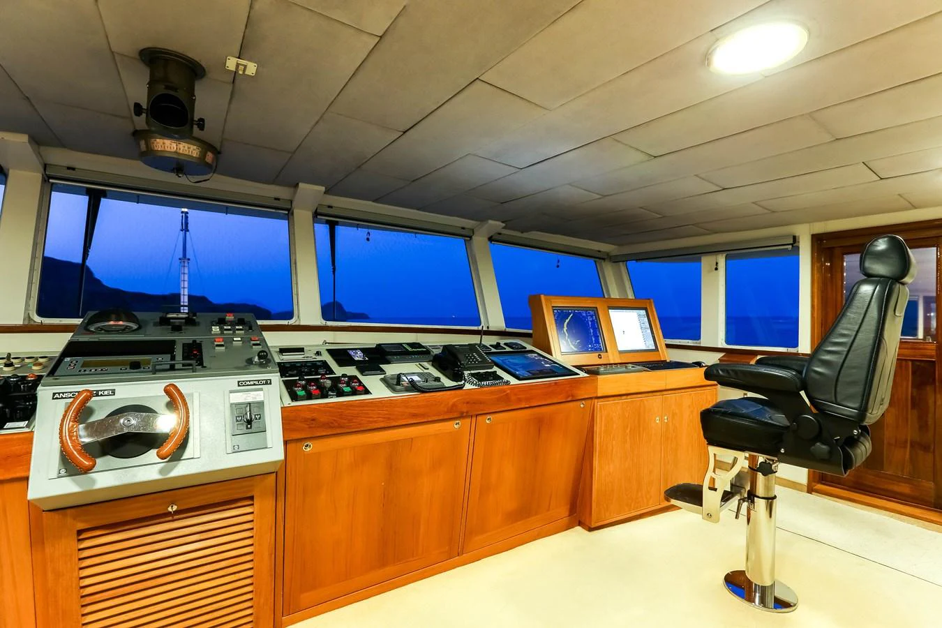 The helm station features advanced navigation equipment and a comfortable captain's chair, set against a backdrop of panoramic windows. aboard ESMERALDA Yacht for Sale