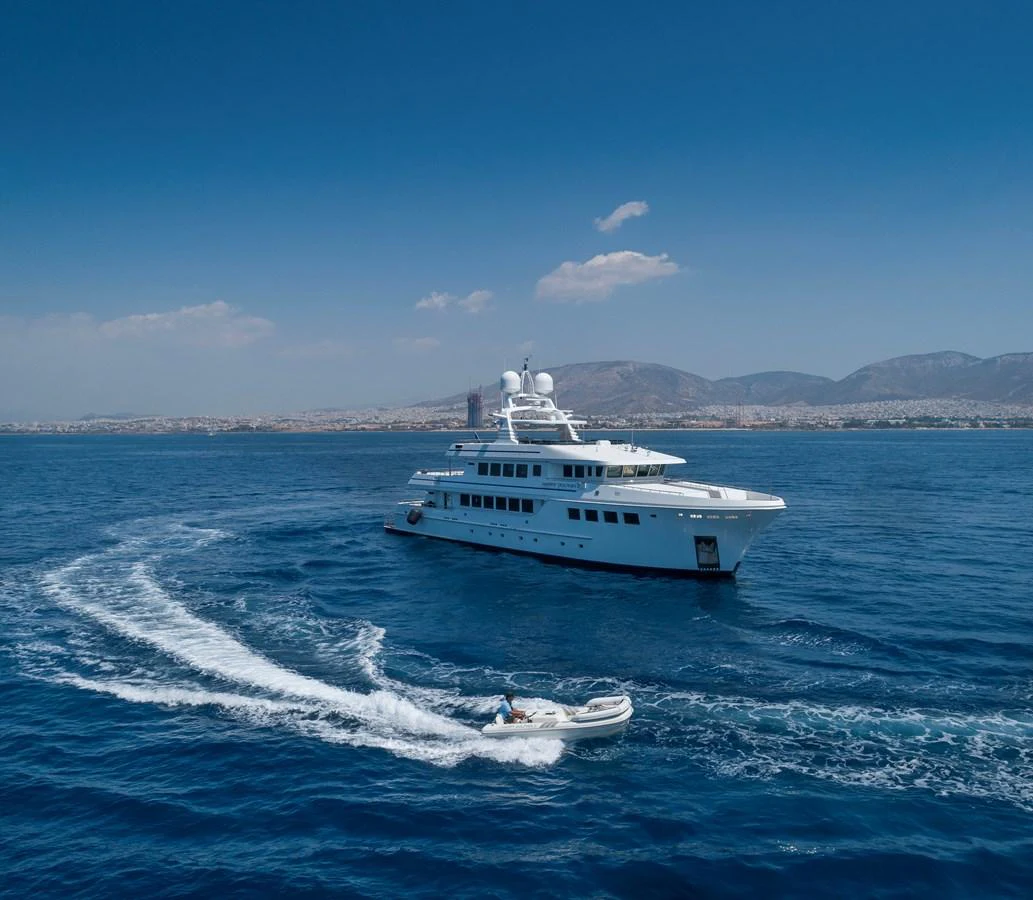 A luxurious yacht cruises through the open sea with a tender boat trailing behind. aboard HAPPY DOLPHIN II Yacht for Sale