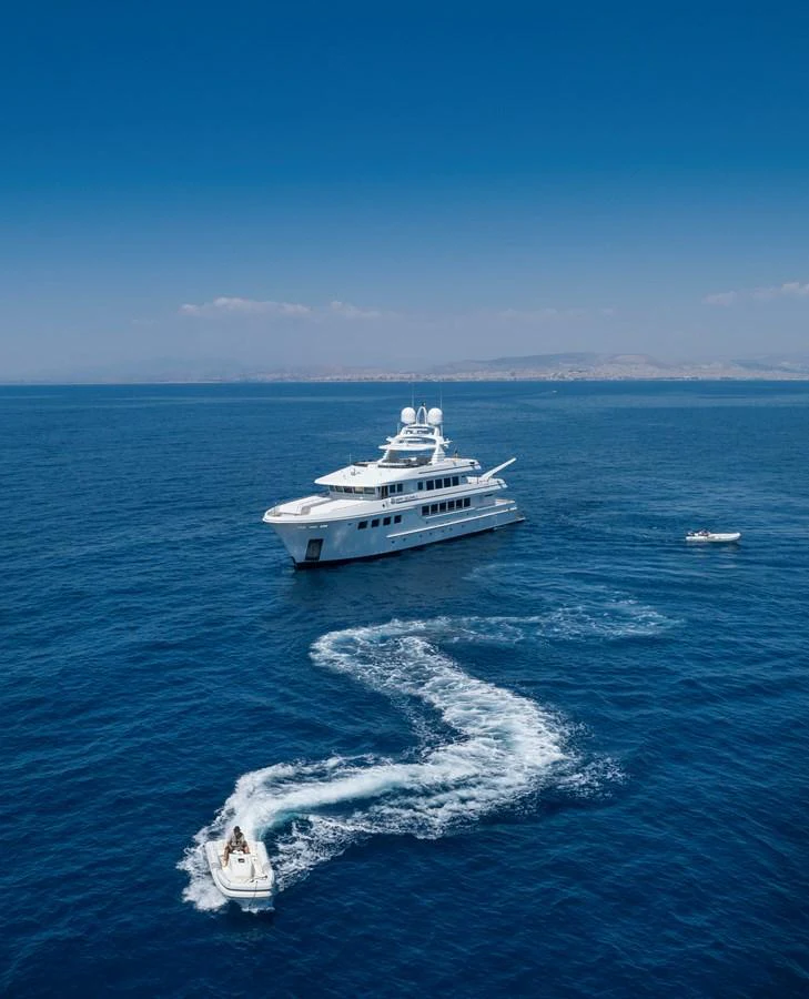 A luxurious yacht cruising on the open sea with a tender boat in the foreground. aboard HAPPY DOLPHIN II Yacht for Sale