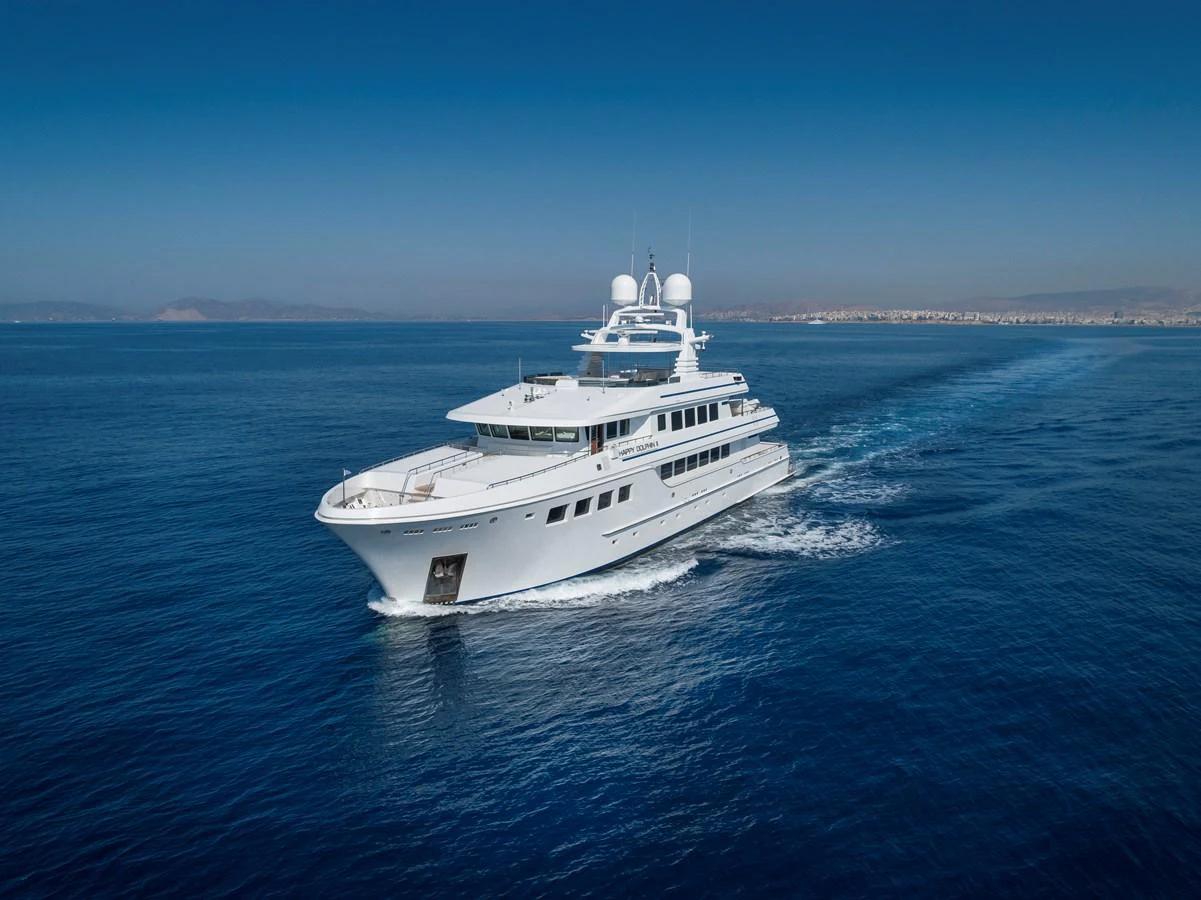 A sleek, modern yacht cruises through calm blue waters under a clear sky. aboard HAPPY DOLPHIN II Yacht for Sale