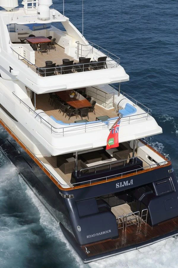 The yacht showcases a spacious aft deck with multiple dining areas, cruising elegantly on the water. aboard SIMA Yacht for Sale