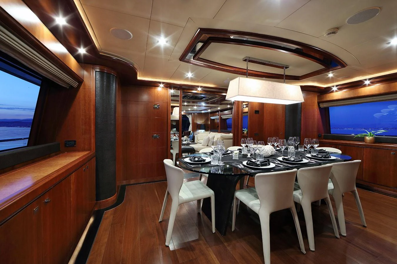 The yacht's dining area features a sophisticated setting with a large table and elegant seating, surrounded by rich wooden finishes. aboard SIMA Yacht for Sale
