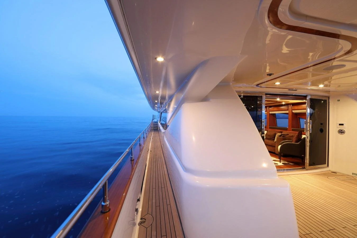 The side deck of the yacht offers a serene view of the open sea, leading to a cozy interior lounge area. aboard SIMA Yacht for Sale