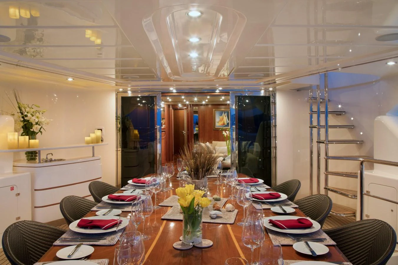 The yacht's dining area is elegantly set for a refined dining experience, featuring a long table with stylish place settings and ambient lighting. aboard SIMA Yacht for Sale